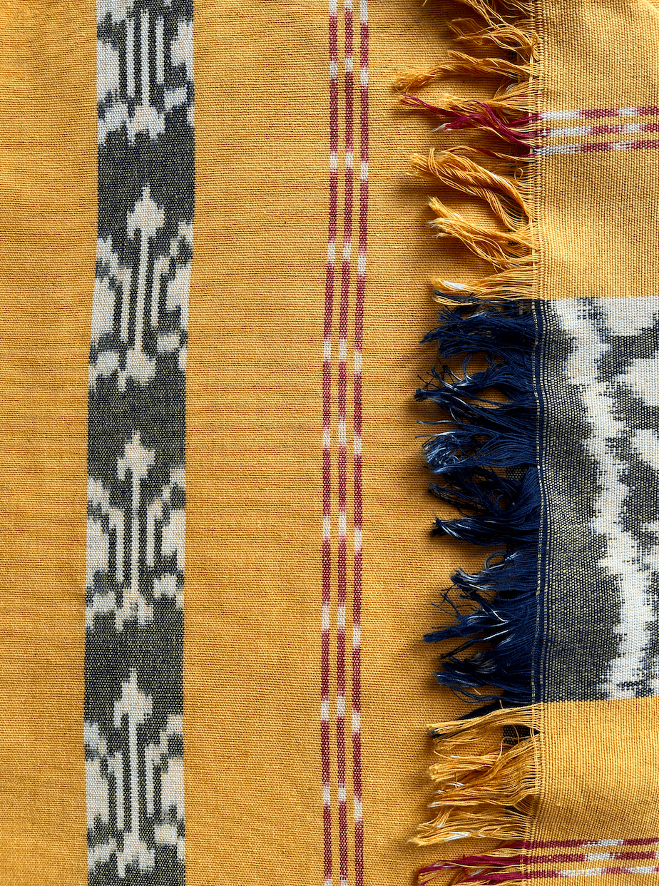 Żółta rękodzielnicza tkanina ikat z czarno-białym geometrycznym wzorem z czerwonym paskiem. Unikalna tkanina wykonana tradycyjną techniką ikat idealnie wpisuje się w trendy rękodzieła i sztuki użytkowej.